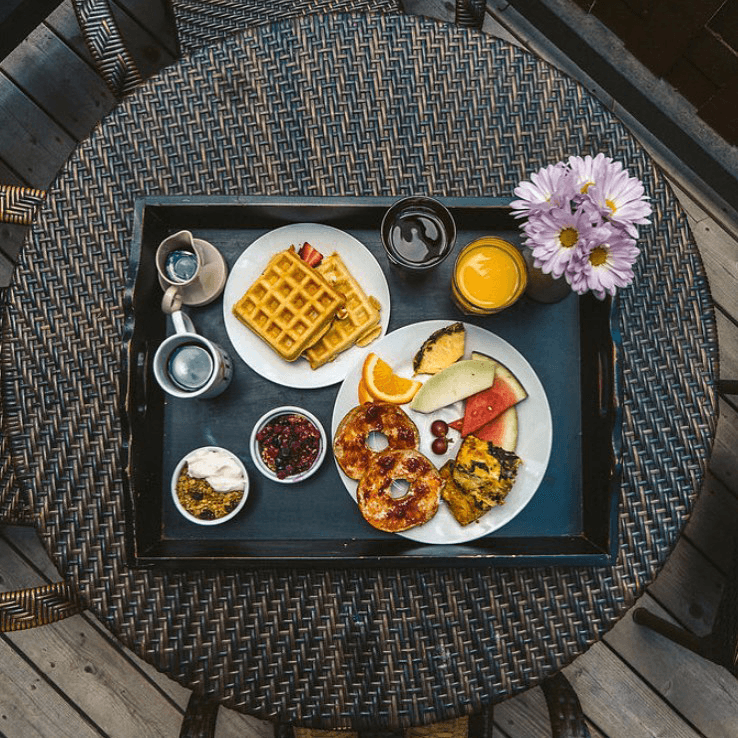 A breakfast tray featuring waffles, fresh fruit, yogurt, and drinks, with a flower accent.