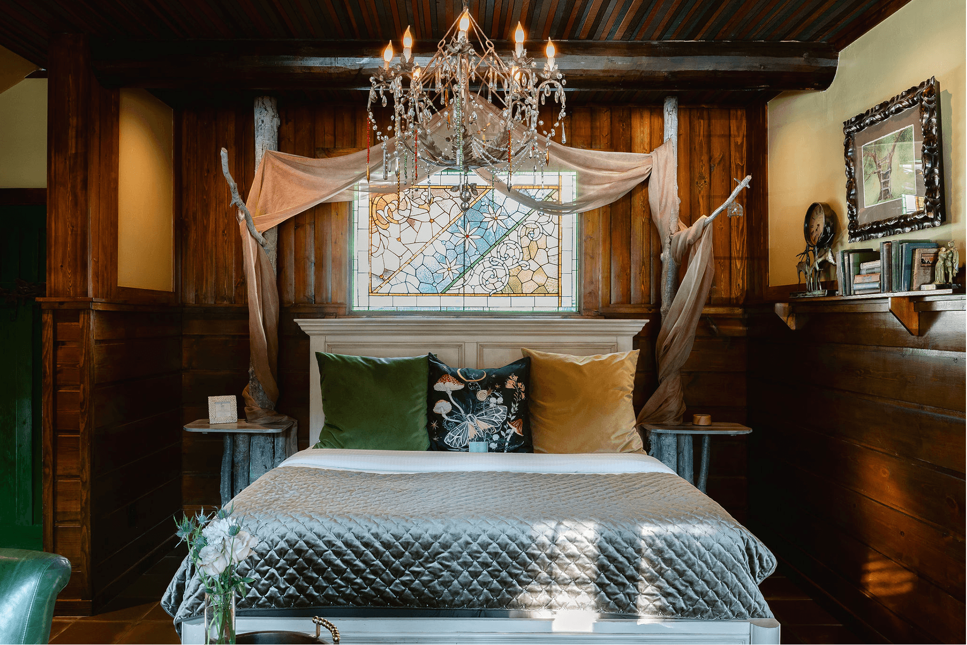 Cozy bedroom featuring a bed with decorative pillows, a quilted blanket, a stained glass window, and a chandelier.