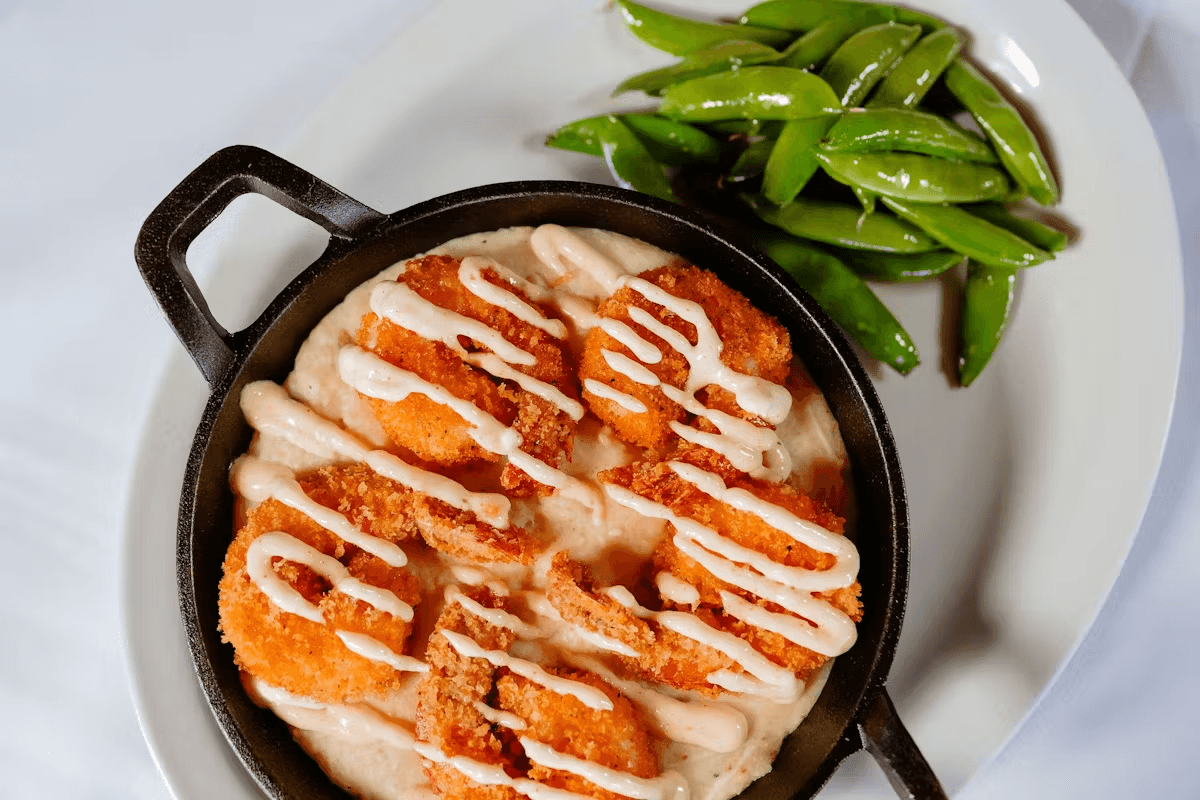 Crispy fried shrimp on a bed of creamy sauce, drizzled with a white sauce, accompanied by green snap peas.