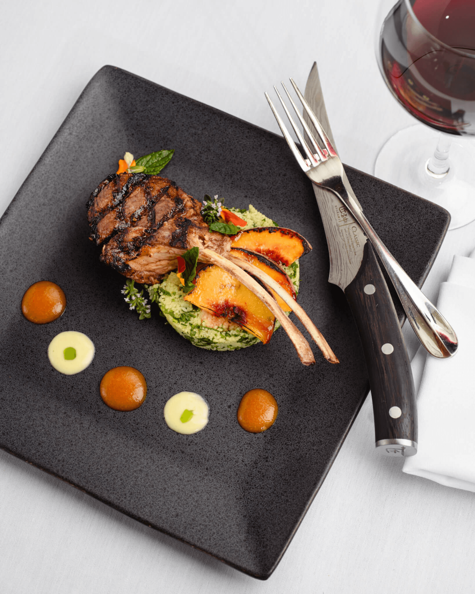 Grilled lamb chops on a bed of green couscous, garnished with peach slices and drizzled sauces.