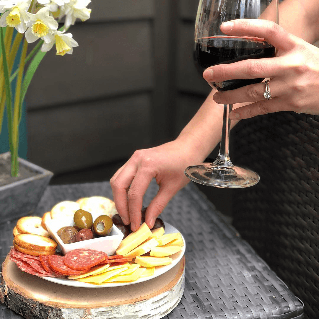 A hand selects cheese from a charcuterie board while the other holds a glass of red wine.