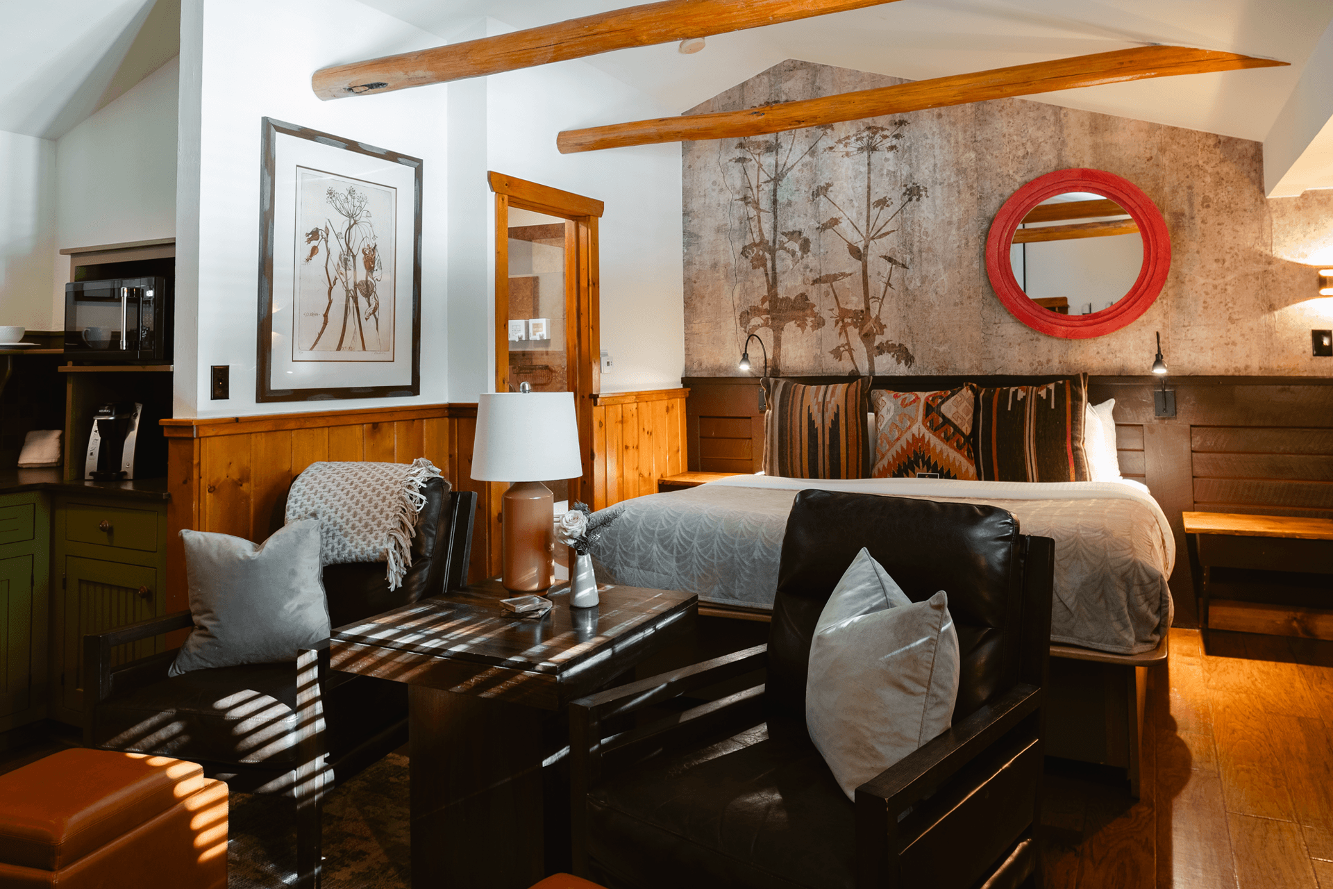 Cozy room featuring a bed with patterned pillows, a seating area, and warm wooden accents.