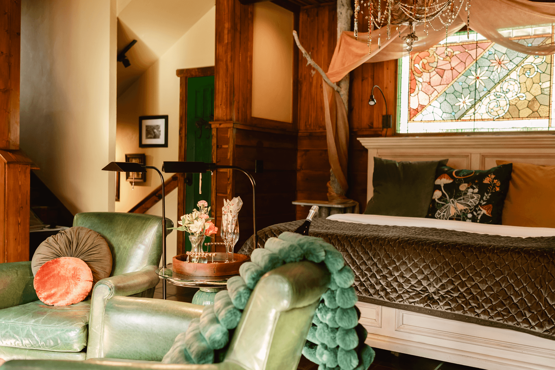 Cozy bedroom featuring green leather chairs, decorative pillows, and a colorful stained glass window.