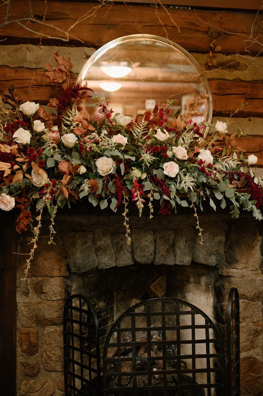 A decorative fireplace mantel adorned with a floral arrangement and a round mirror above it.