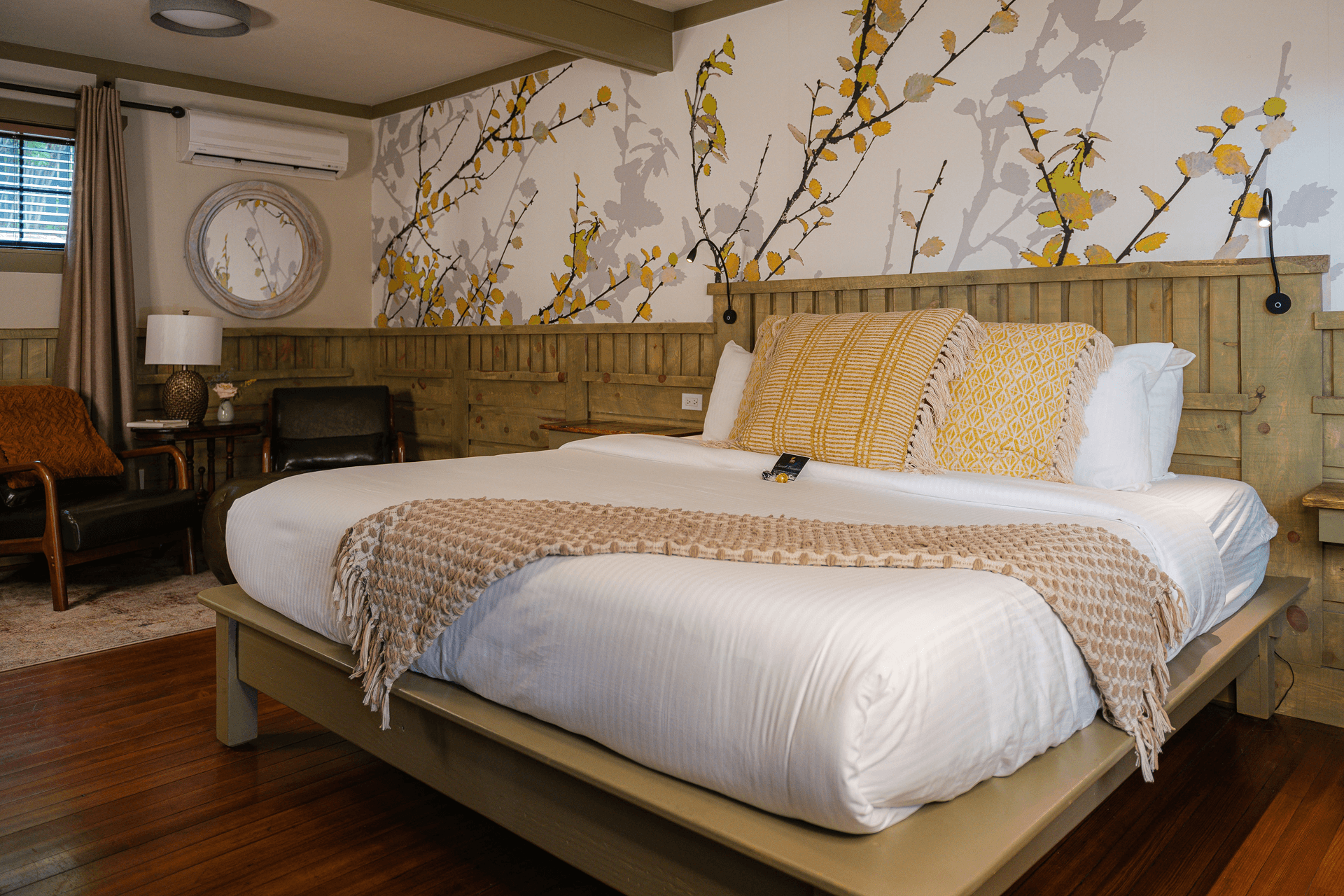 A cozy bedroom featuring a large bed with decorative pillows, a green armchair, and floral wallpaper.