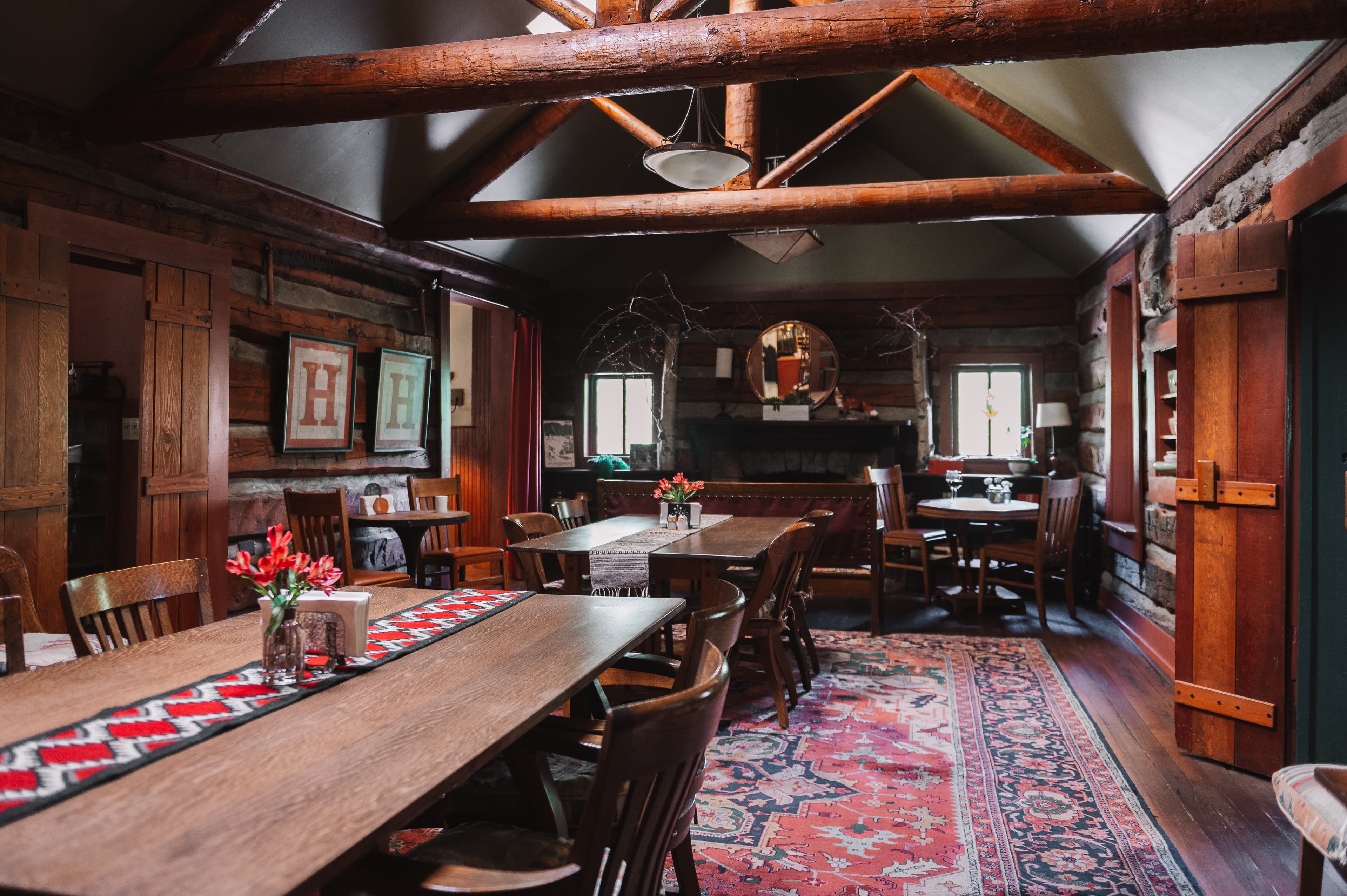 A cozy, rustic dining area with wooden tables, chairs, and a decorative rug.