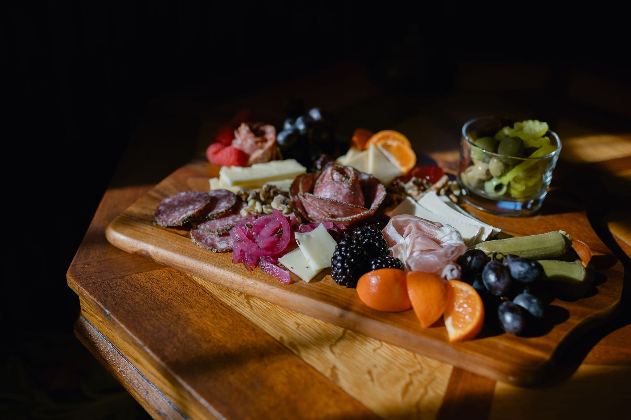 A wooden charcuterie board featuring assorted meats, cheeses, fruits, and pickles.