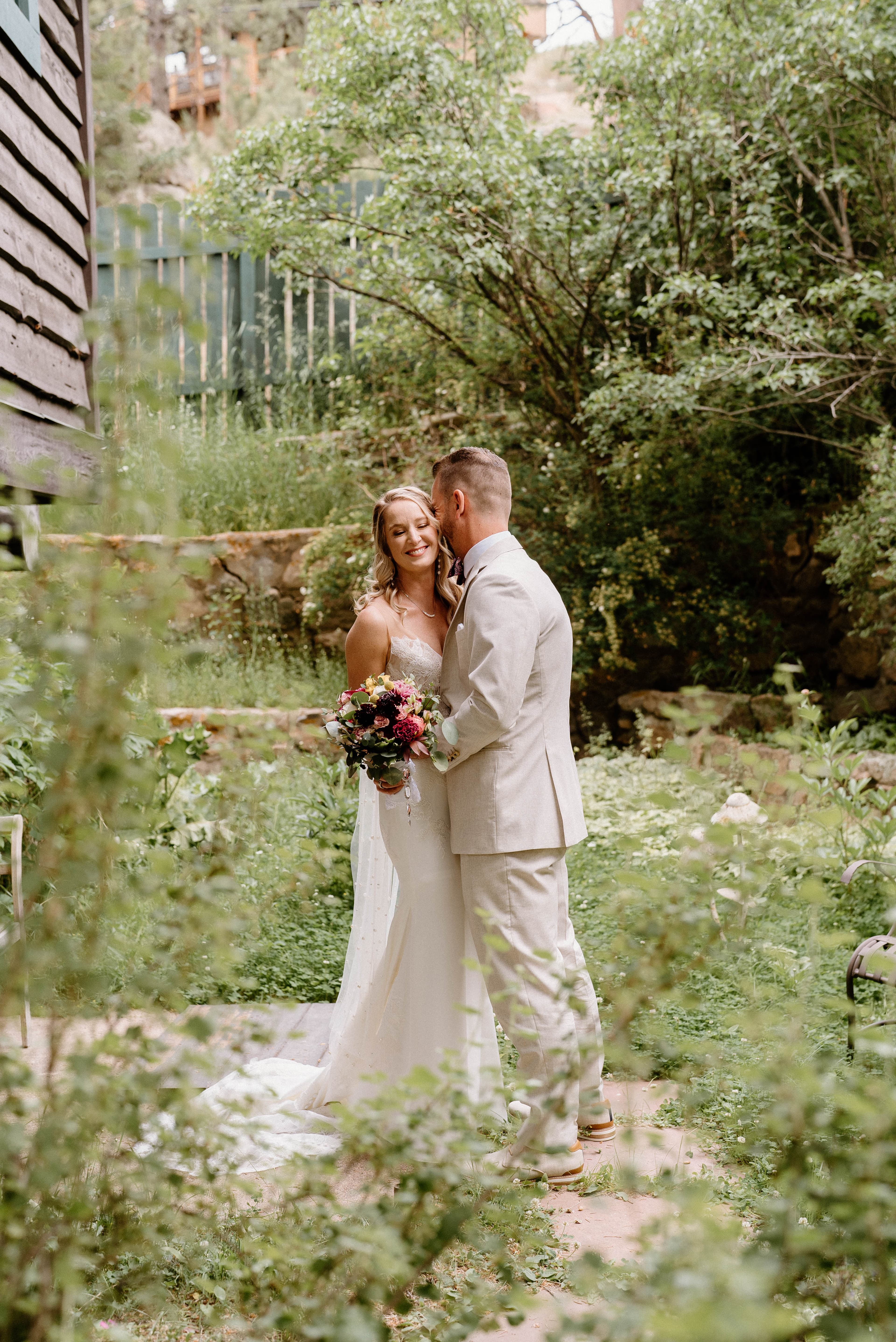 A smiling couple embraces in a lush garden, surrounded by greenery.