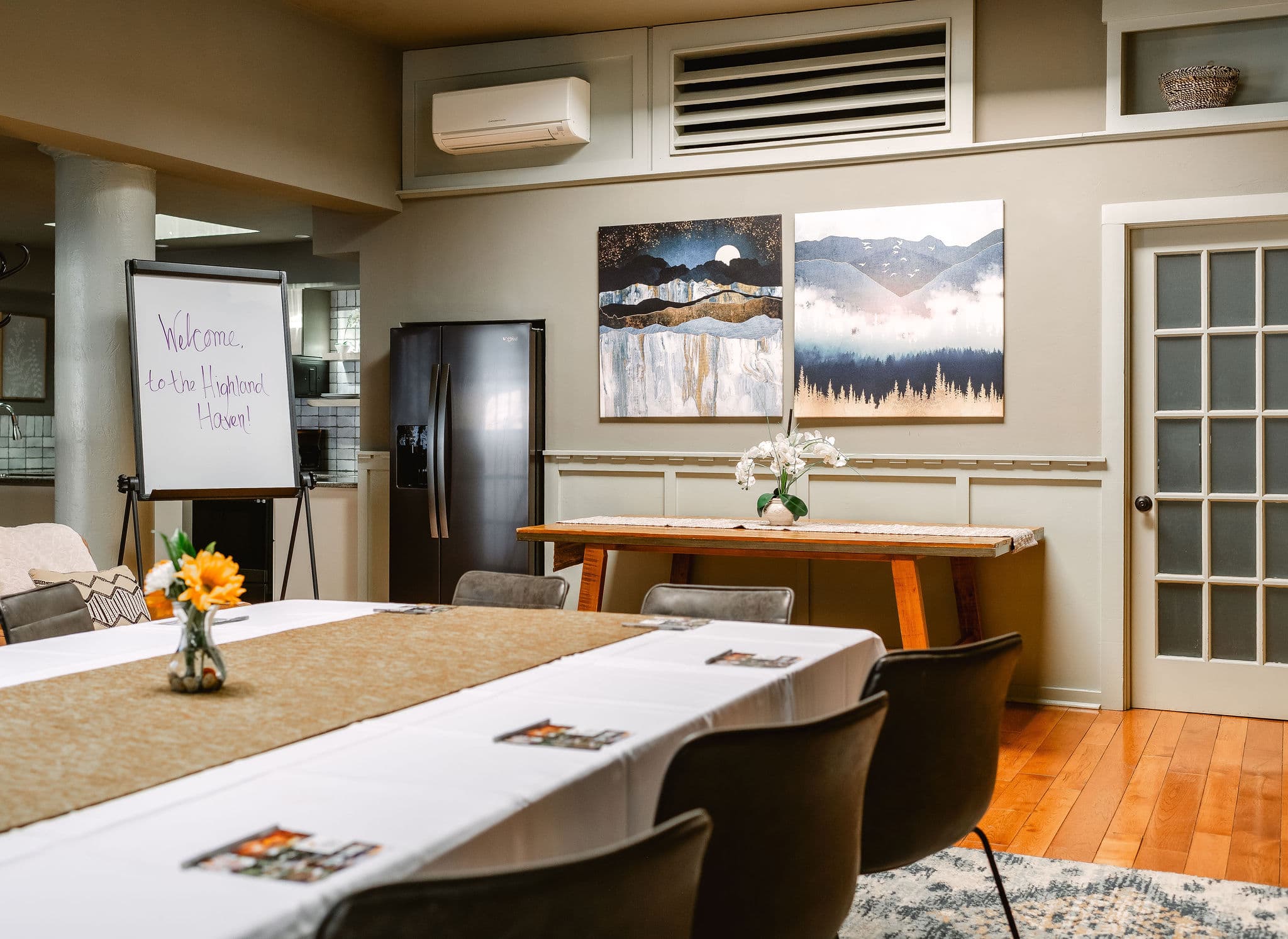 A welcoming meeting room featuring a table set for guests, artwork on the walls, and a sign greeting attendees.