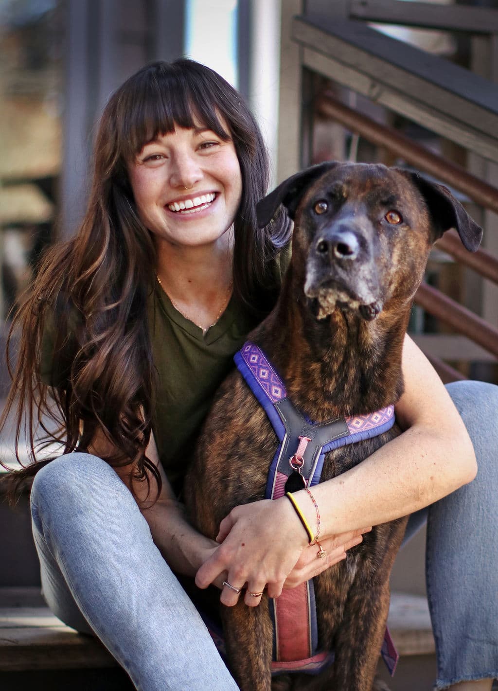 A woman with long hair smiles while sitting with her brown and black dog.