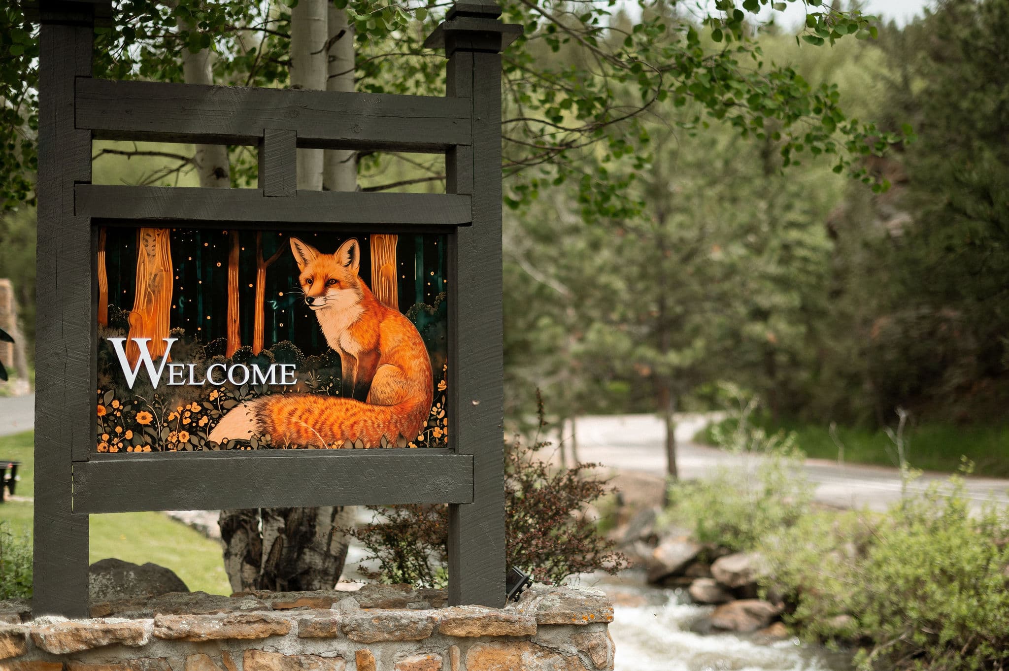 A welcoming sign featuring a painted fox among trees and the word "Welcome."