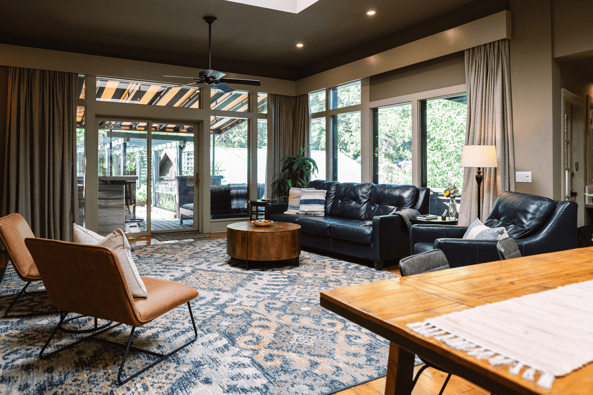 A cozy living room featuring leather sofas, stylish seating, and large windows that open to an outdoor view.