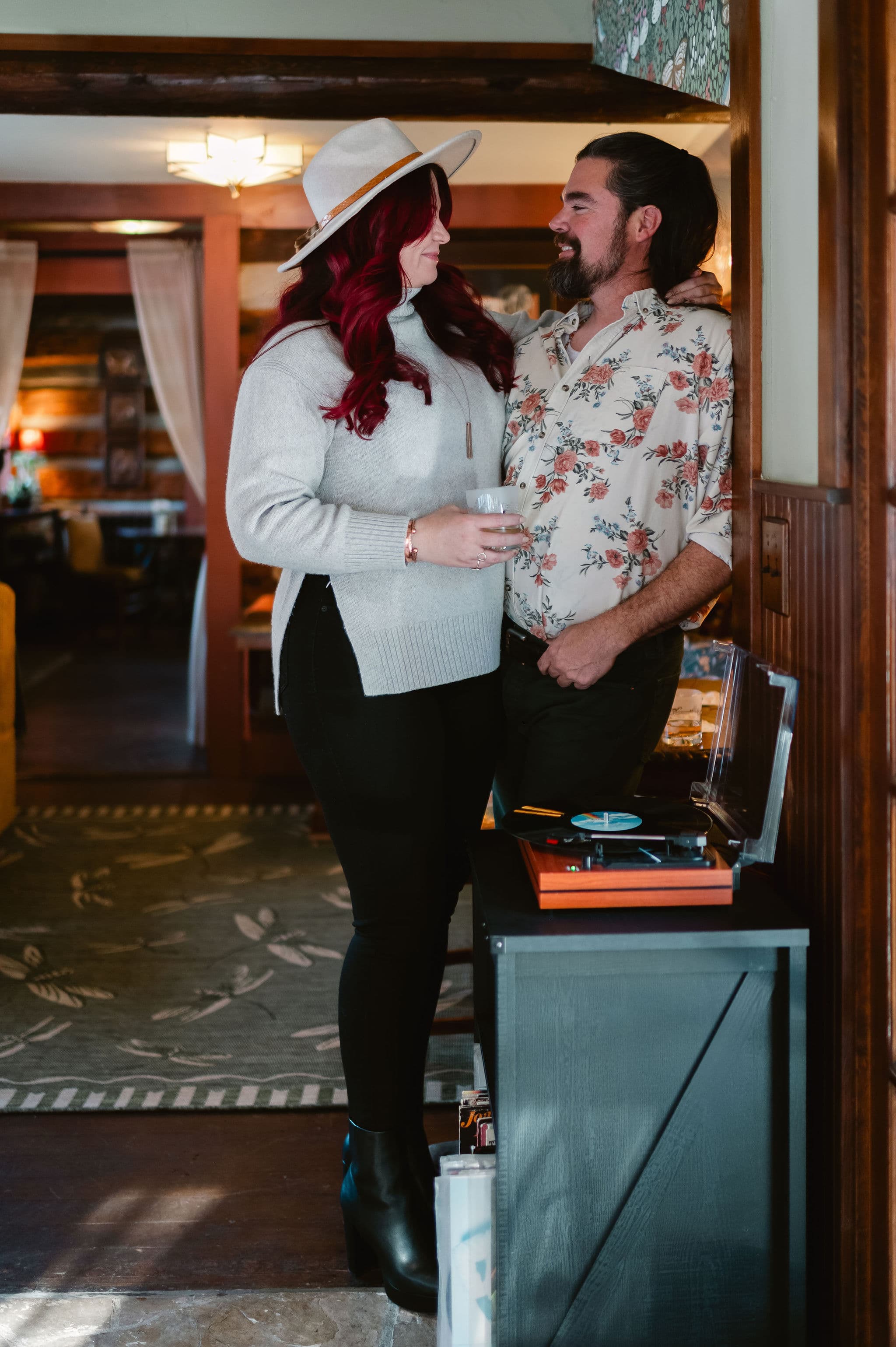 A couple shares a tender moment indoors, with one partner holding a drink and both smiling at each other.