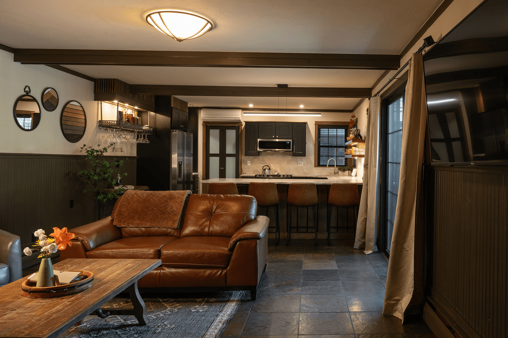 A cozy living room featuring a brown leather couch, a wooden coffee table, and an open kitchen with modern appliances.