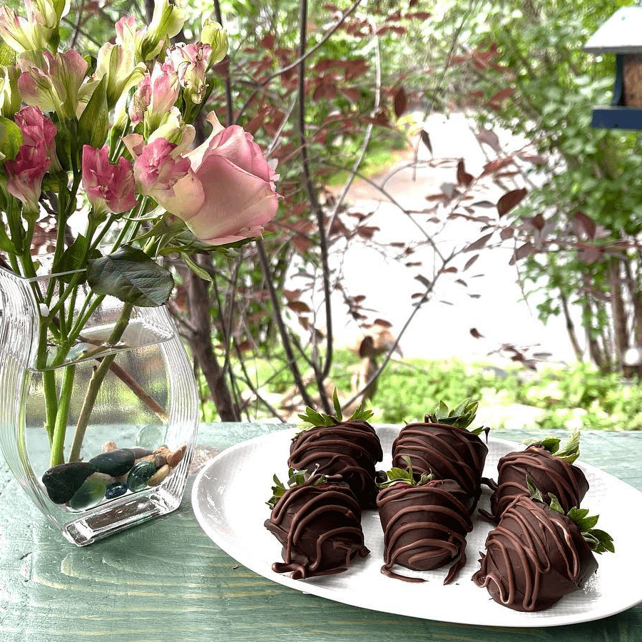 A plate of chocolate-covered strawberries next to a vase of flowers.