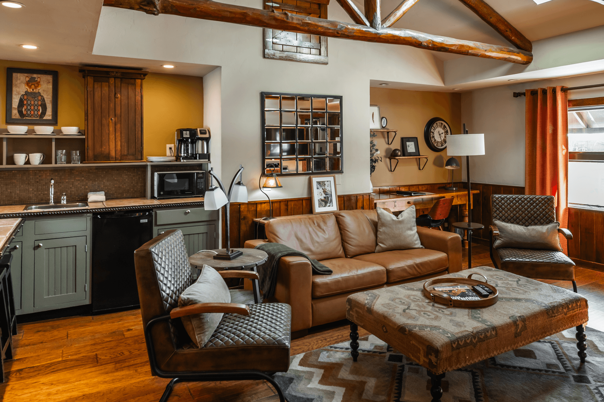 A cozy living area featuring a leather sofa, patterned ottoman, and a compact kitchenette with wood accents.