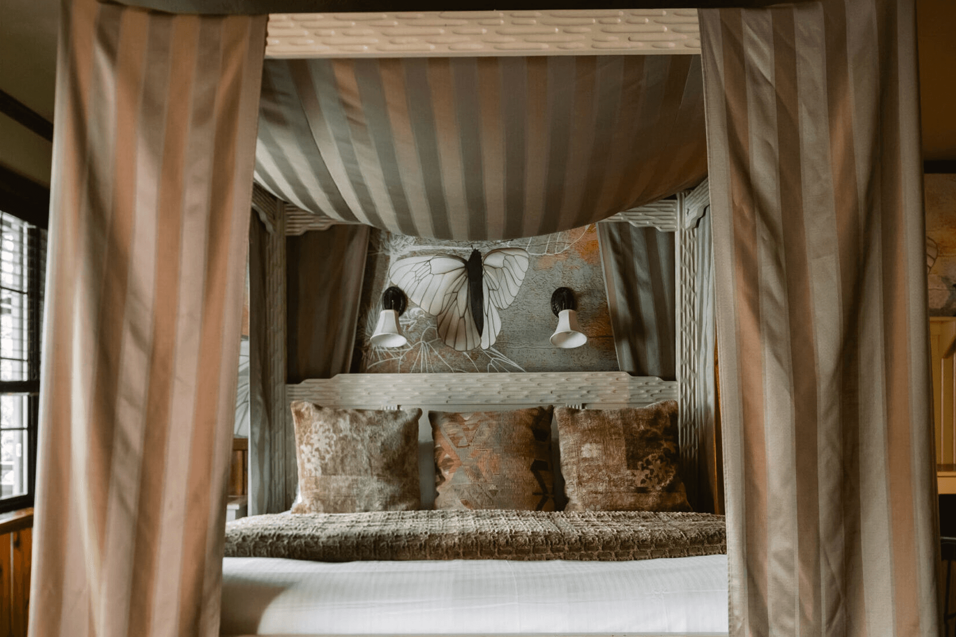 A cozy, stylishly decorated bed surrounded by elegant drapes and wall art featuring a butterfly.