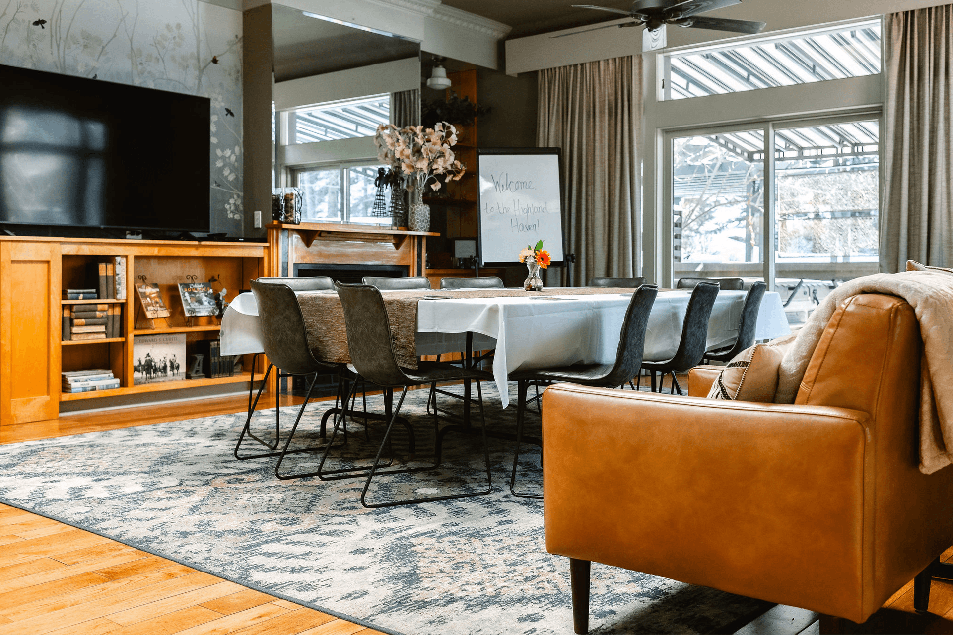 A cozy conference room with a table set for a meeting. Eight chairs surround the table with a whiteboard that reads "Welcome." Sunlight streams in.